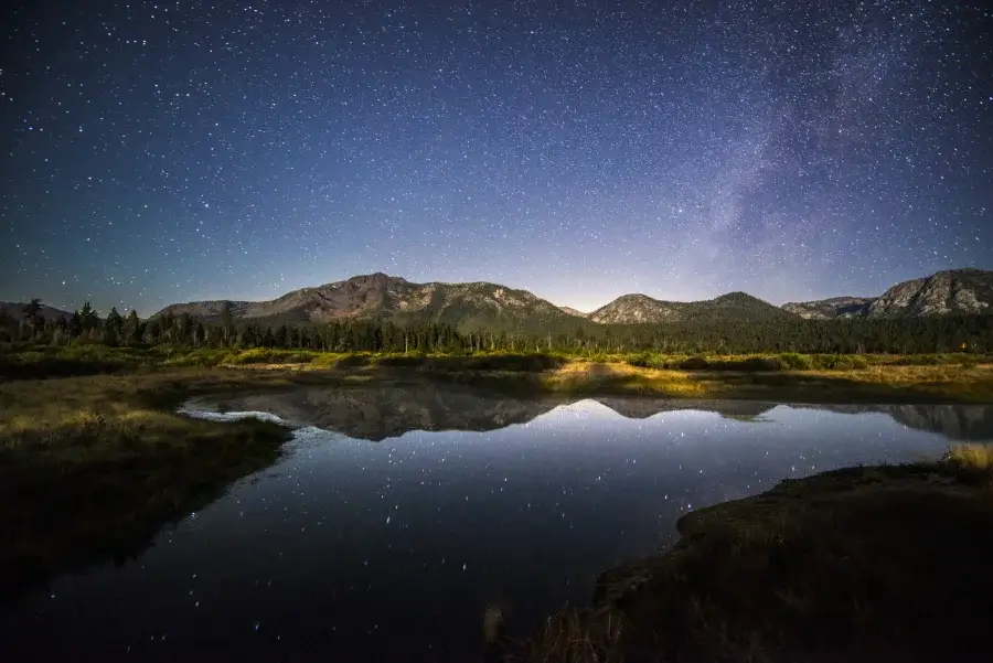 A scenic shot of the night sky over Mount Tallac, with the mountain range reflecting on the lake