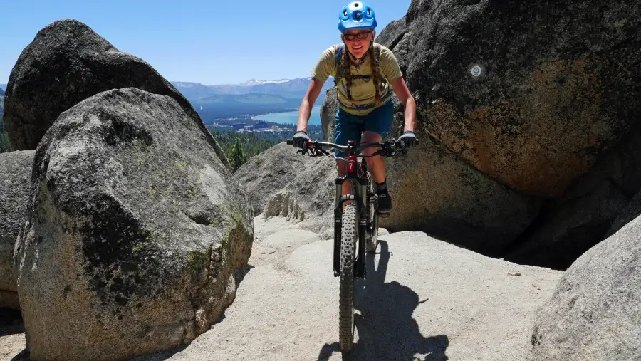 Young woman riding her mountain bike through boulders with views of Lake Tahoe in the background